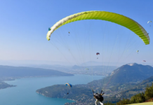 En un día soleado en un valle cerca de un río una persona está aprendiendo a cómo volar en parapente con un parapente verde.