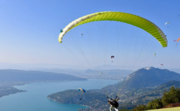 En un día soleado en un valle cerca de un río una persona está aprendiendo a cómo volar en parapente con un parapente verde.