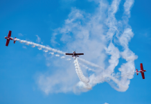 Tres personas disfrutando de su regalo de vuelo acrobático en aviones rojos en un cielo despejado.