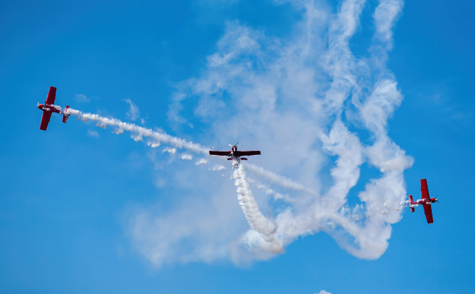 Tres personas disfrutando de su regalo de vuelo acrobático en aviones rojos en un cielo despejado.