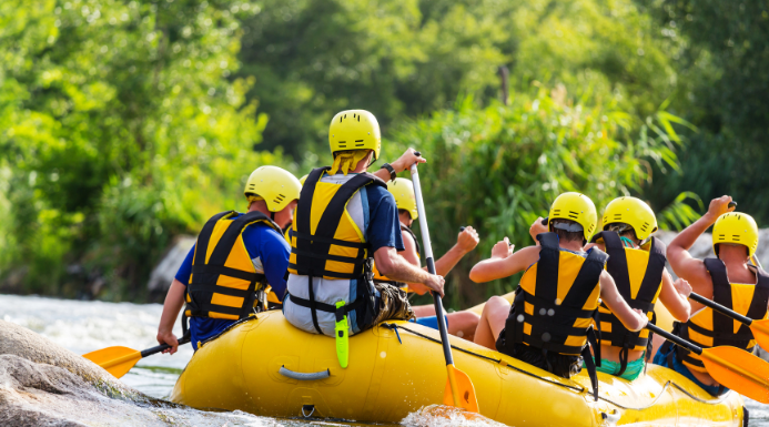 Un grupo de personas están haciendo rafting en Huesca con el equipamiento necesario, casco, chaleco salvavidas, remo y bote todo de color amarillo.